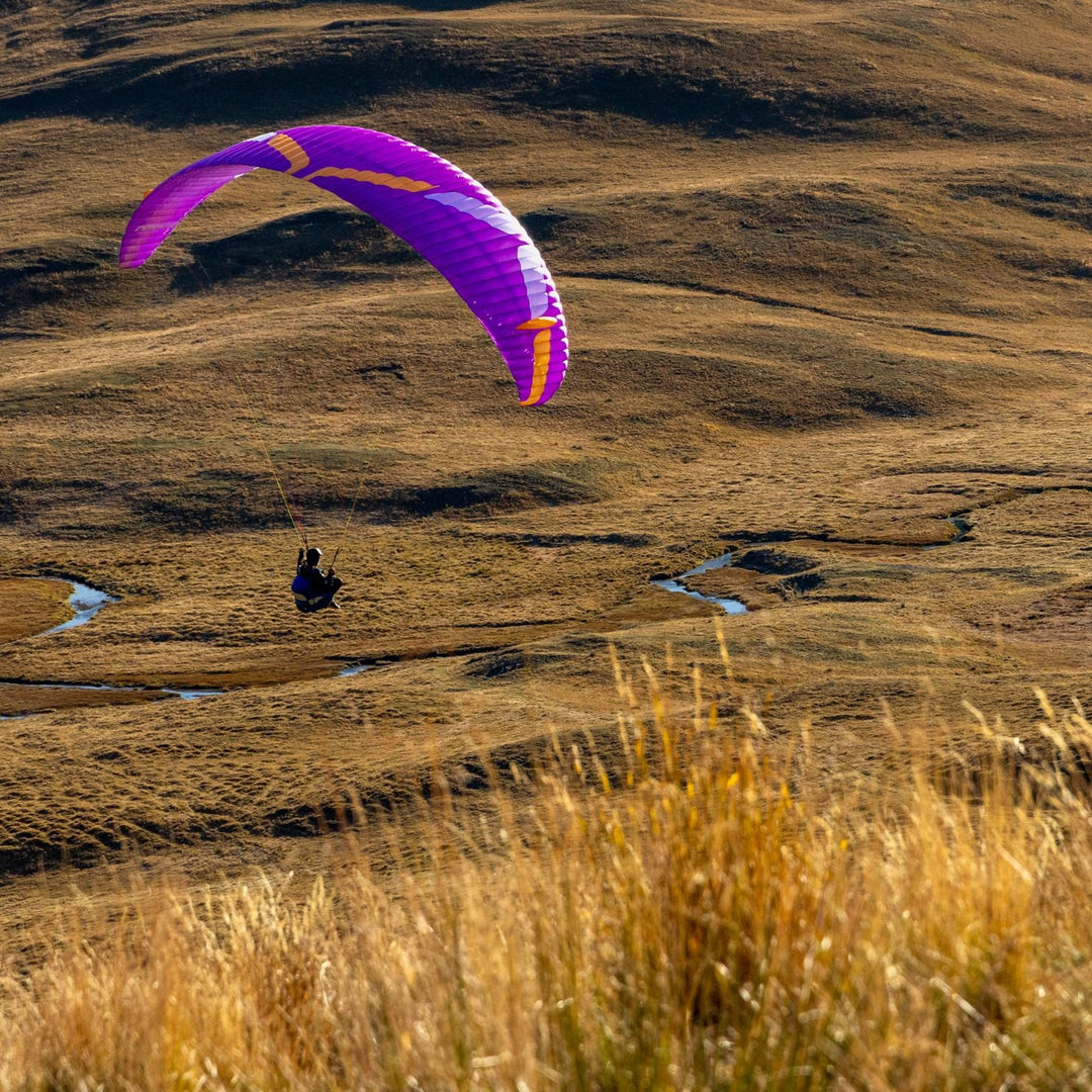 Person paragliding over a vast, open landscape with a purple parachute.