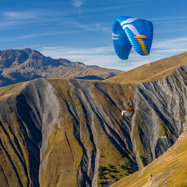 Paraglider flying over a mountainous landscape with a blue parachute.