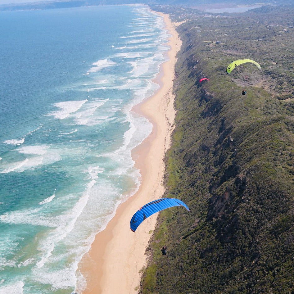 3 Flow Future paragliders flying side by side along the stunning coastline of Paradise ridge in Wilderness